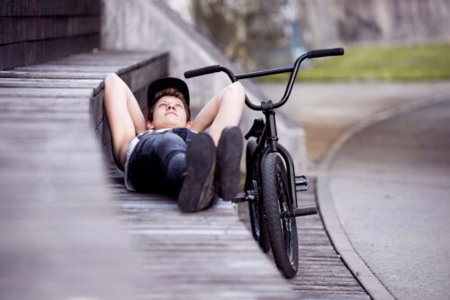 Teenager lies next to their bike deep in thought.