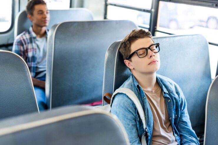 A boy is asleep on a school bus.
