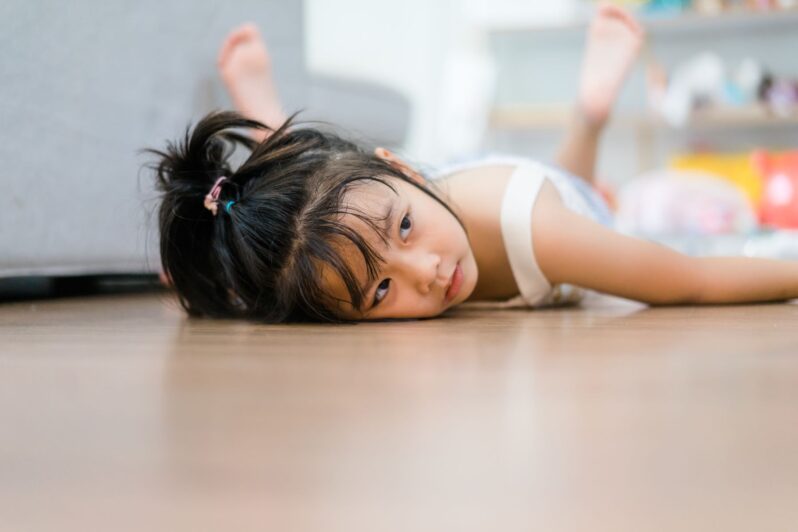 A child is bored and lying on the floor.