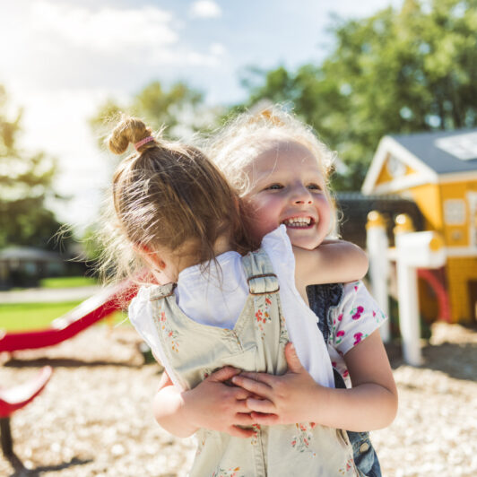Two kids hugging and playing on the playground.