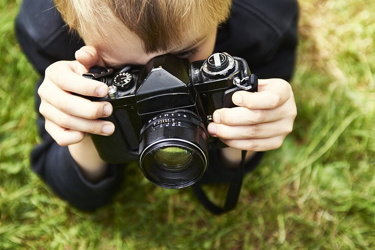 A boy with a film camera photographs outside.