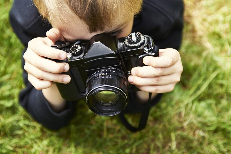 A boy with a film camera photographs outside.