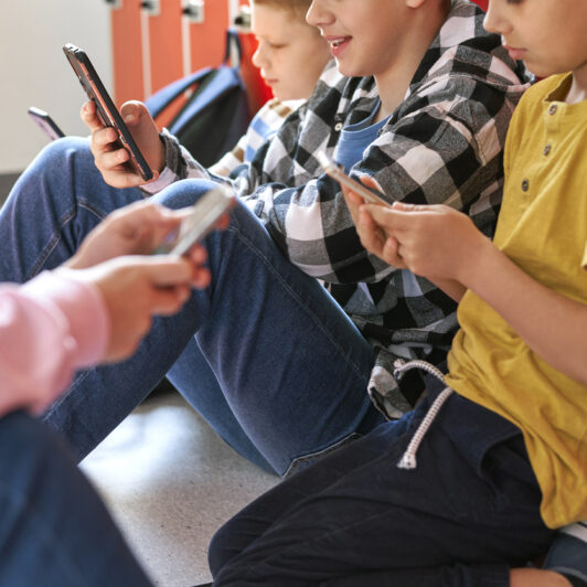 Adolescents sitting on the floor in school looking at their smartphones.