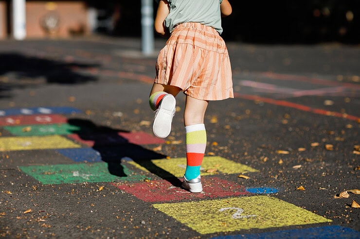 A girl plays hopscotch drawn on the ground with colorful chalk.