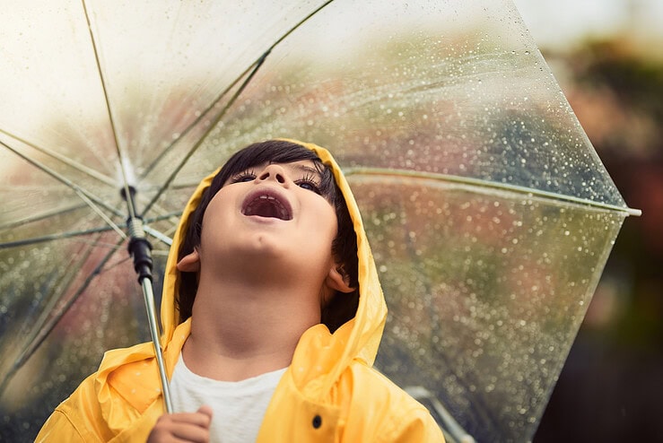 A boy is looking up at the sky on a rainy day while holding an umbrella.
