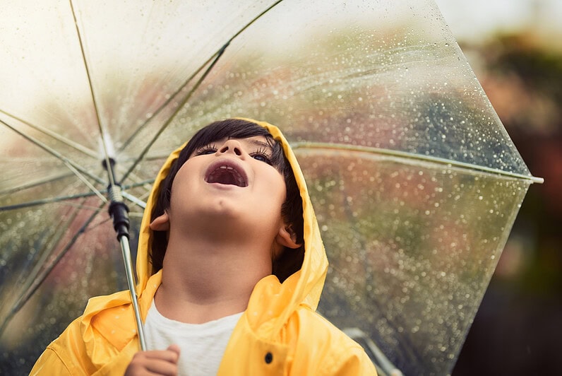 A boy is looking up at the sky on a rainy day while holding an umbrella.