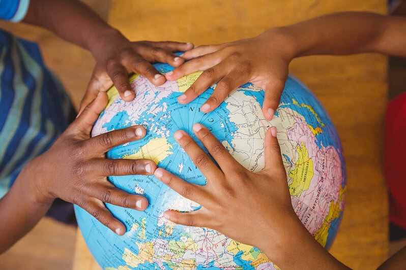 Children's hands are on a globe in a classroom.