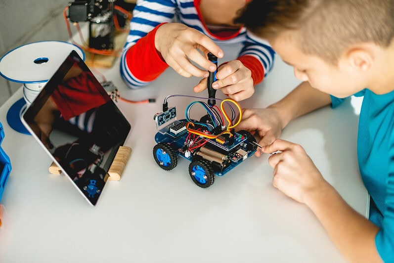 Two kids fix a small robotic car toy together.