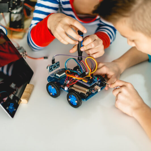 Two kids fixing a small robotic car toy together.