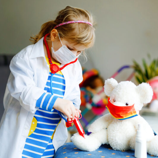 A little girl is playing pretend with a toy stethoscope and a toy syringe.