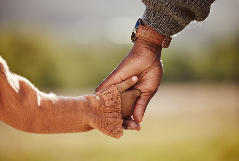 A child holds hands with her parent.