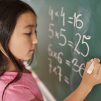 A girl is completing a maths equation on a chalkboard.