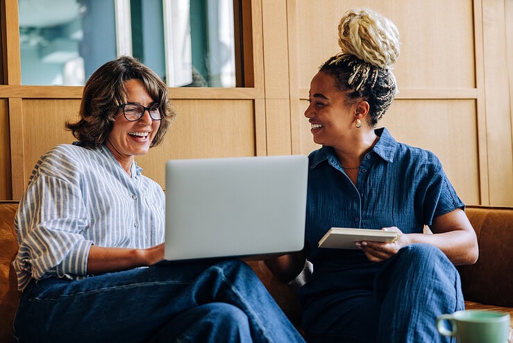 Two teachers are having a discussion in front of an open laptop.