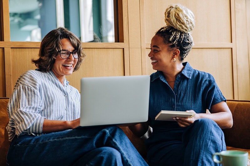 Two teachers are having a discussion in front of an open laptop.