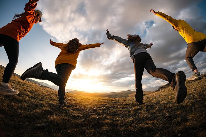 A group of teenagers running towards the sunset together.