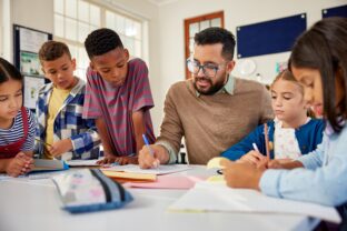 A teacher helps a group of young students with their schoolwork at a classroom table.