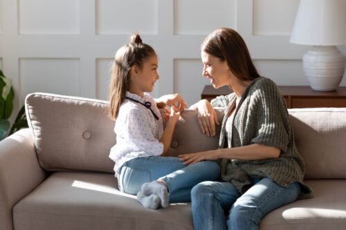 A mother and a daughter are sitting on a couch having a conversation.