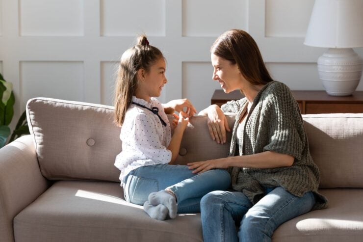 A mother and a daughter are sitting on a couch having a conversation.