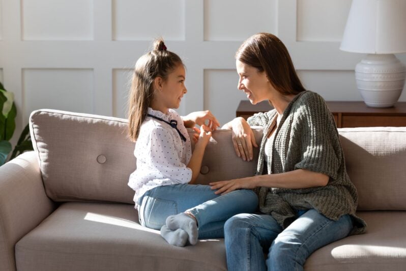 A mother and a daughter are sitting on a couch having a conversation.