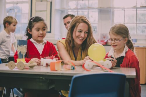 A teacher is sitting with two children doing a creative project.