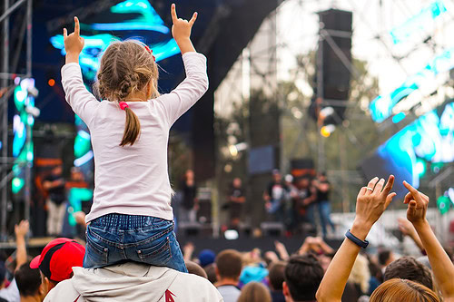A child sits on their parent's shoulders at a concert.