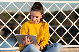 A child sits outside, working on a tablet.
