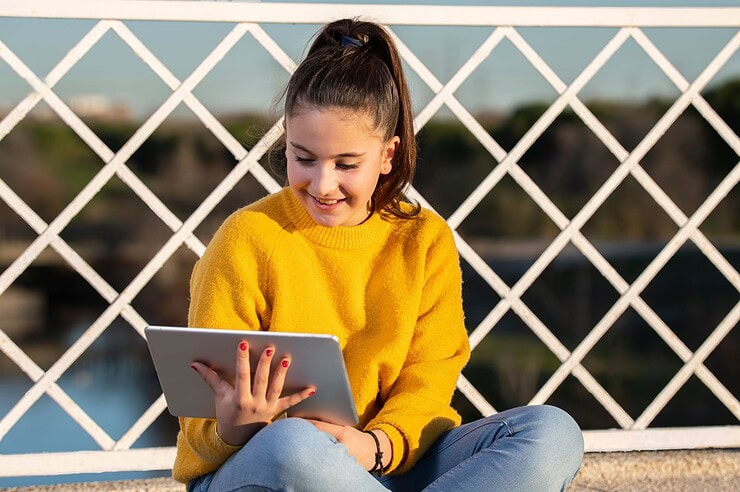 A child sits outside, working on a tablet.