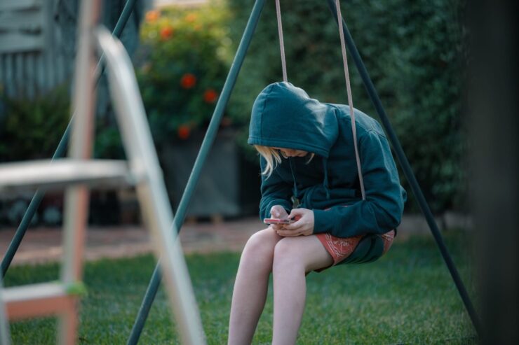 A teen sits on a swing looking at their phone.
