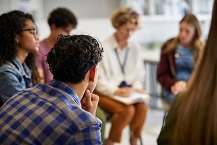 An adult and teenagers are sitting in a circle having a discussion.