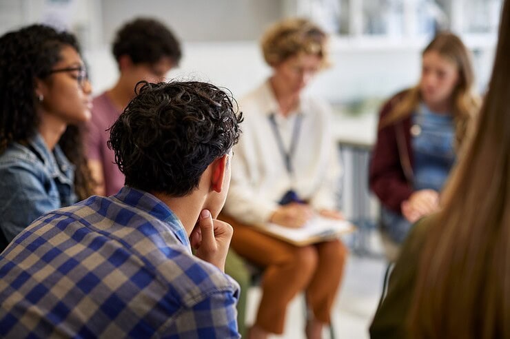 An adult and teenagers are sitting in a circle having a discussion.