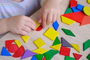 A child plays with colored wooden geometric figures.