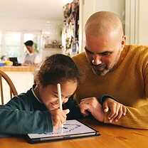 A child and parent work on a tablet together.
