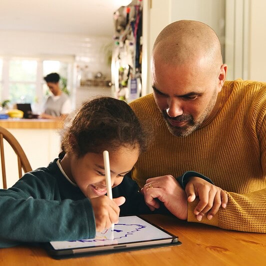 A child and parent work on a tablet together.