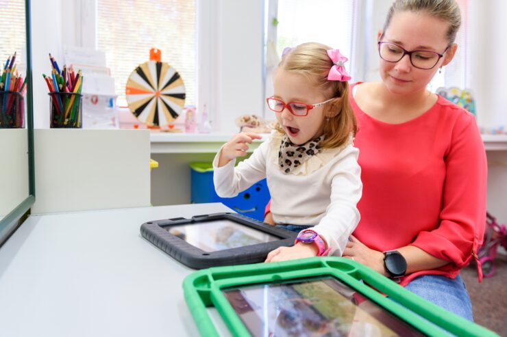 An adult is helping a child use a tablet.