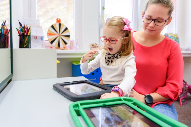 An adult is helping a child use a tablet.