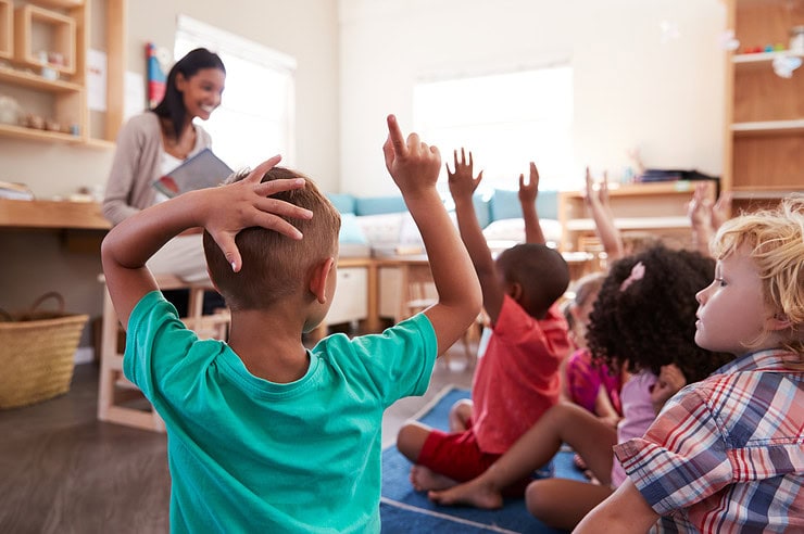 Children in a classroom raise their hands to answer a teacher's question.