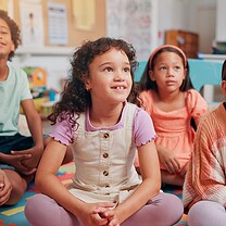 Children sitting on the classroom carpet look attentive.