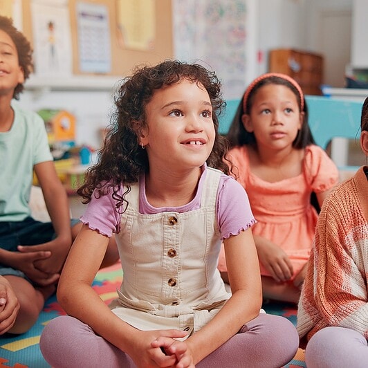Children sitting on the classroom carpet look attentive.